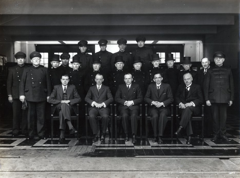Foto van het personeel van de firma Innemée, genomen in de deuropening van de garage aan de Hooikade 43-36, die in 1932 in gebruik werd genomen. De naam Innemée leeft voort in Monuta’s Haagse uitvaartcentrum Monuta Innemee. (Collectie Museum Tot Zover)